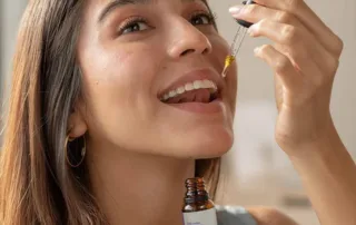 Woman taking a dropper full of CBD Tinctures while holding the bottle.