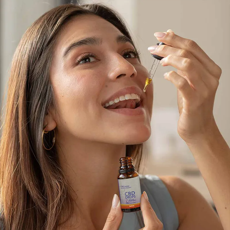 Woman taking a dropper full of CBD Tinctures while holding the bottle.