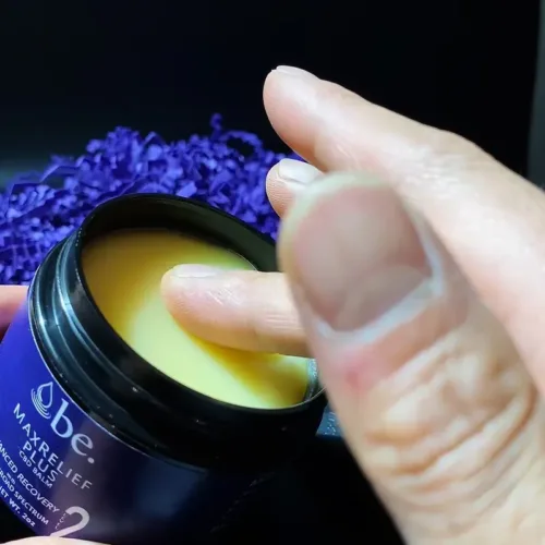 A hand skimming the top of a jar of CBD balm.