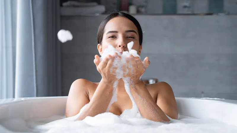 A woman in a bubble bath playing with bubbles.