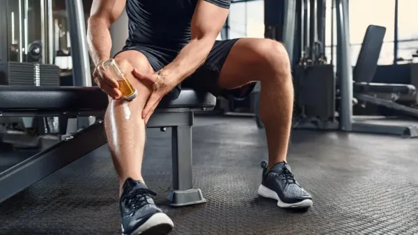 A man at a gym applying a pain relief to his knees.