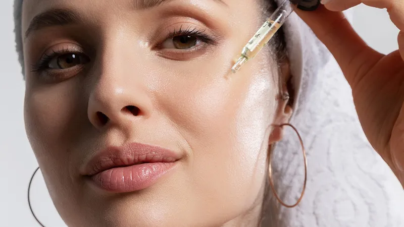 A woman applying a facial serum to her cheek.